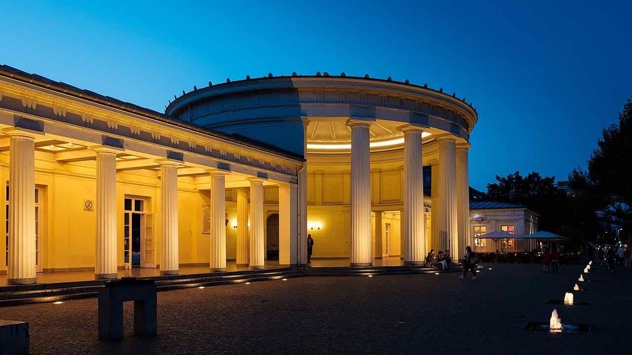 The columned rotunda of the Elisenbrunnen lit yellow against a deep blue evening sky