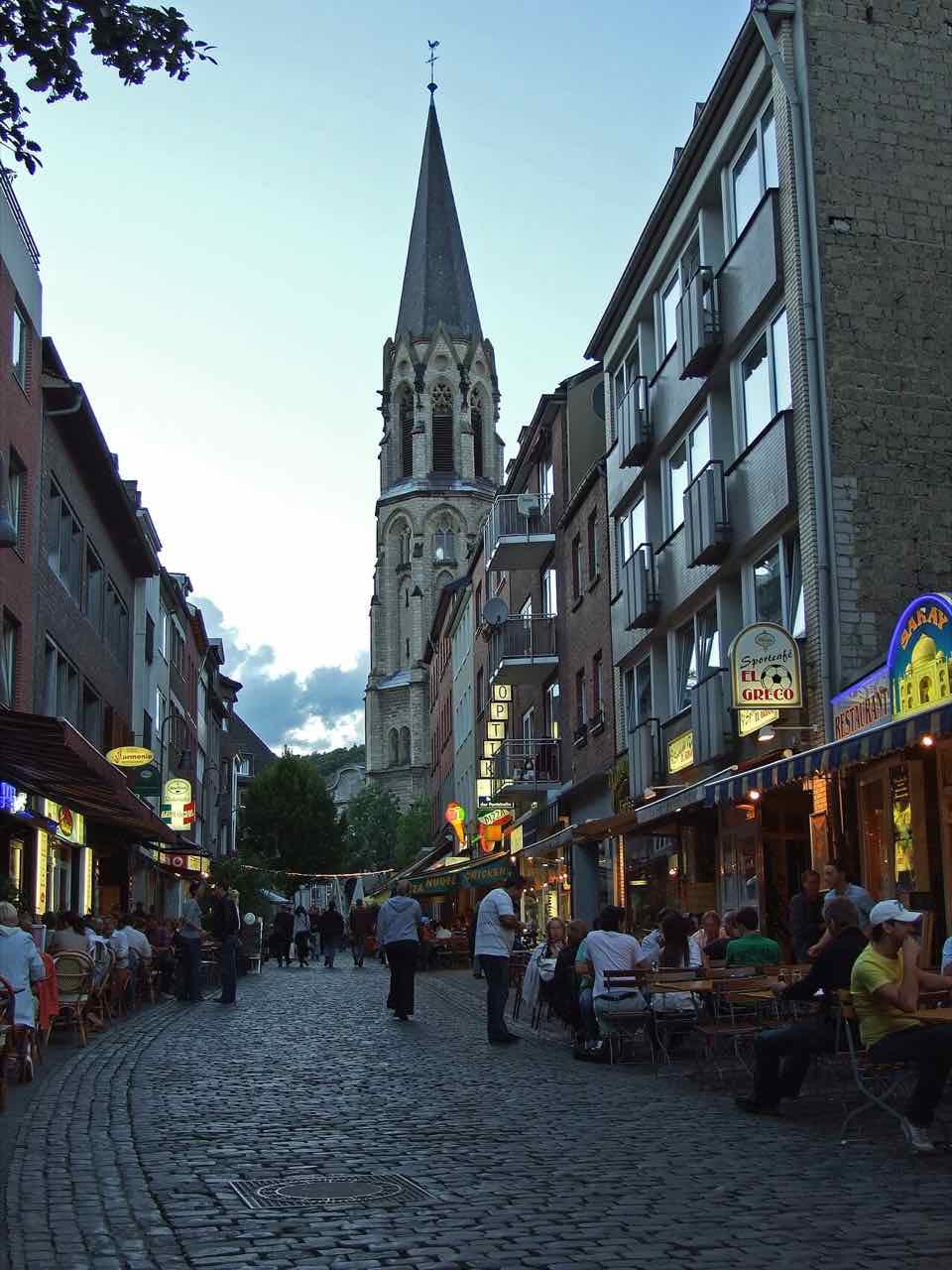Pontstraße at dusk with people at restaurant tables on the cobbles and a church spire at the end of the street