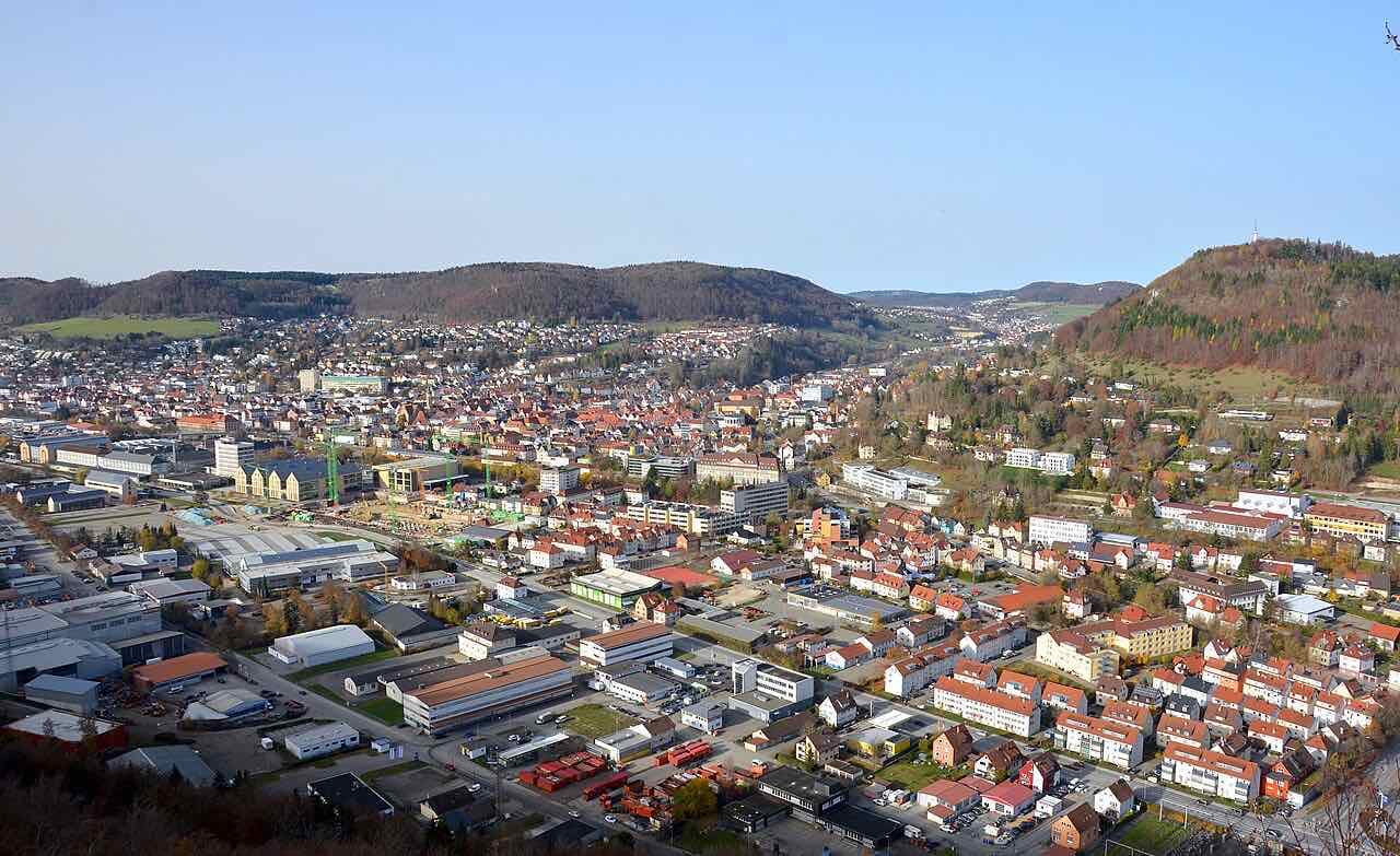 View over the roofs and factory buildings of Ebingen in an autumn valley, with wooded hills behind and a transmitter mast on the hill at the right