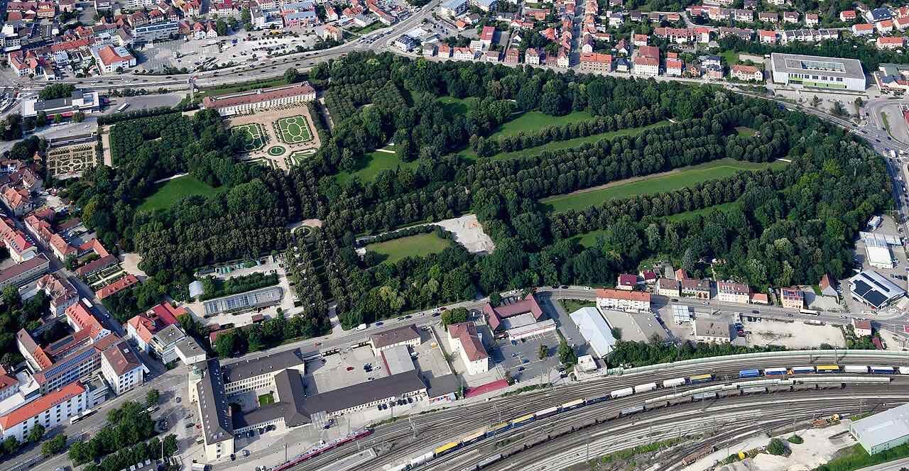 Aerial view of the Hofgarten in Ansbach: a large green park with tree-lined avenues, the Orangerie at the top, houses around it and the railway tracks along the bottom edge