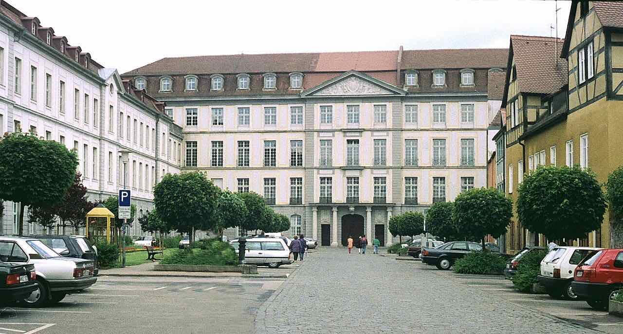 The Reitbahn square in Ansbach with cobbled paving, clipped trees, a half-timbered house on the right and a large pale Baroque building behind