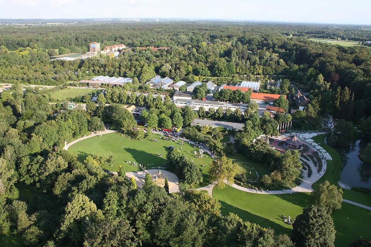 An aerial view of the Augsburg Botanical Garden with its lawns, paths and glasshouses surrounded by dense woodland