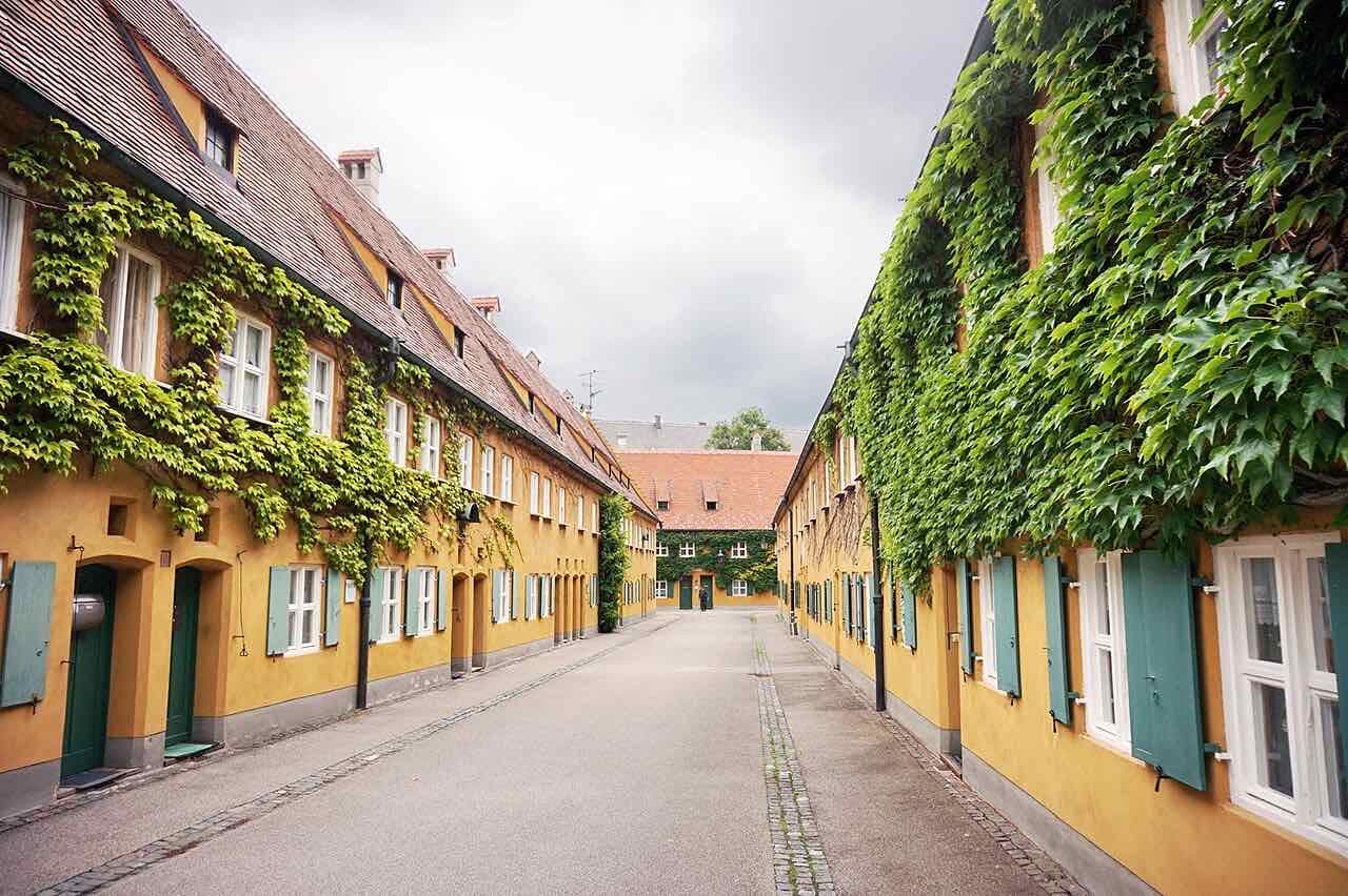 A quiet lane in the Fuggerei, lined with ochre houses with green shutters and ivy on the walls