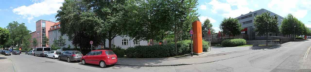 A street corner at the Technical University of Applied Sciences Augsburg with an orange sign pillar, trees and university buildings