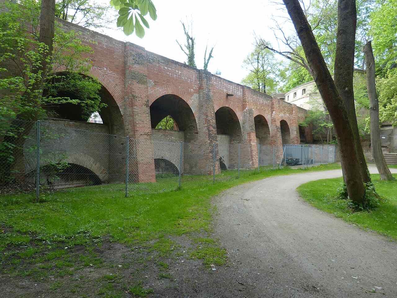 The brick arches of the aqueduct at the Rotes Tor beside a gravel path and trees