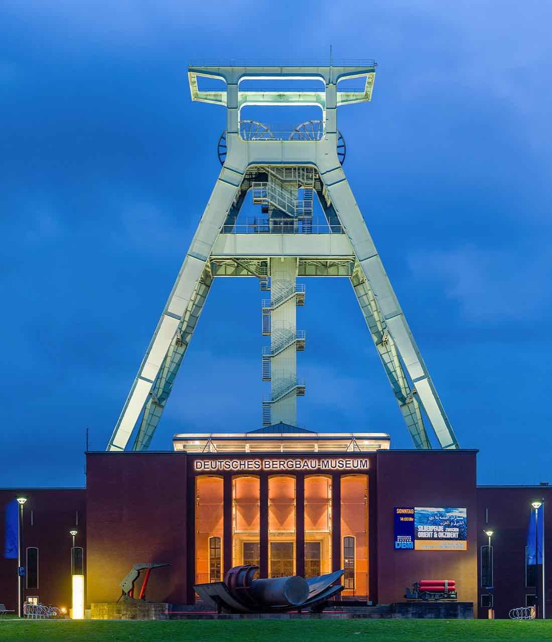 The steel headframe of the Deutsches Bergbau-Museum lit up at blue hour above the museum entrance in Bochum