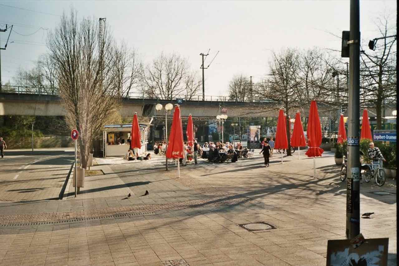 Red parasols over café tables on a sunny spring afternoon in the Bermudadreieck pub district, with a railway viaduct behind
