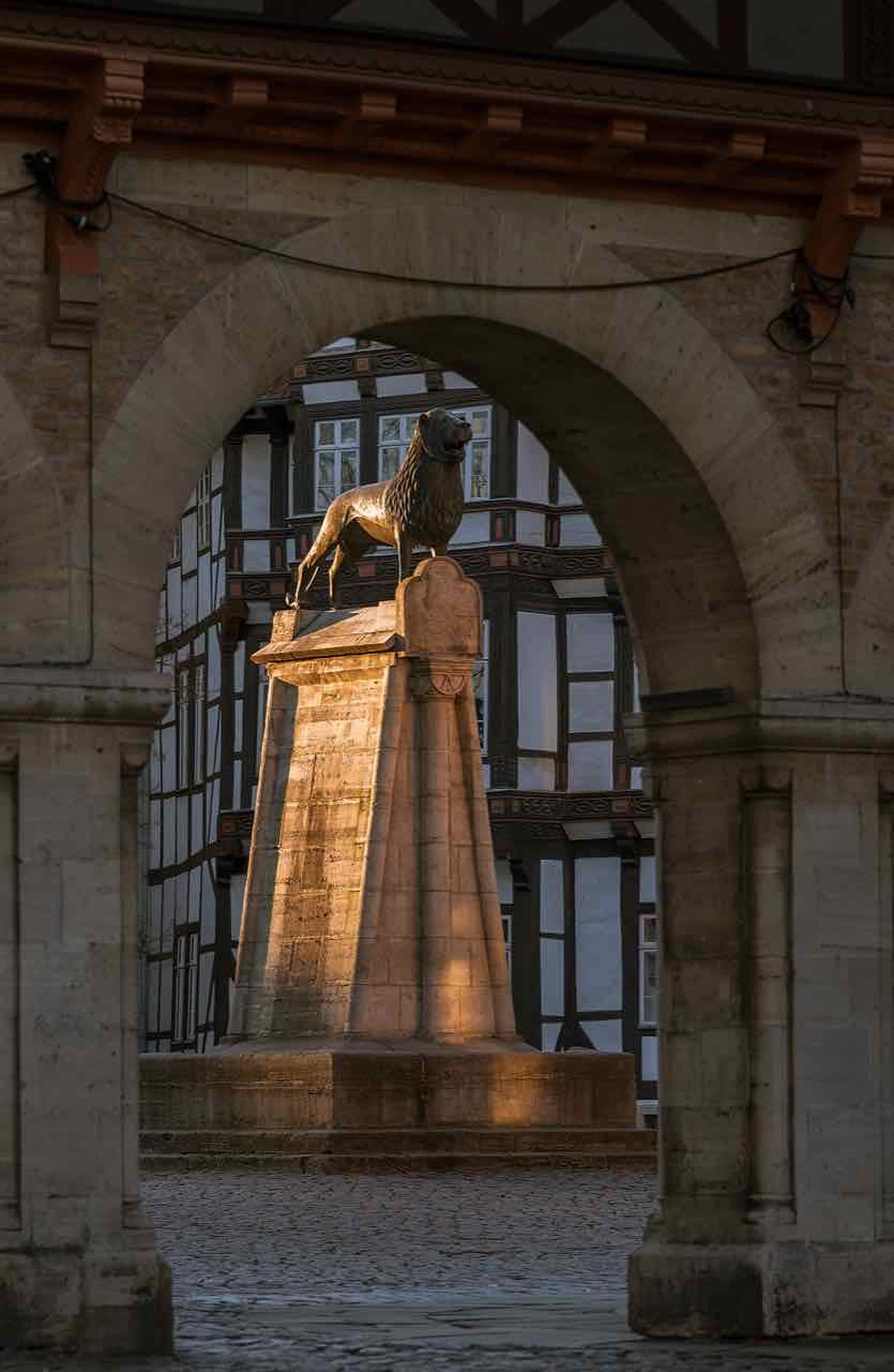 The bronze Brunswick lion on its stone plinth seen through a stone arch, with half-timbered houses behind
