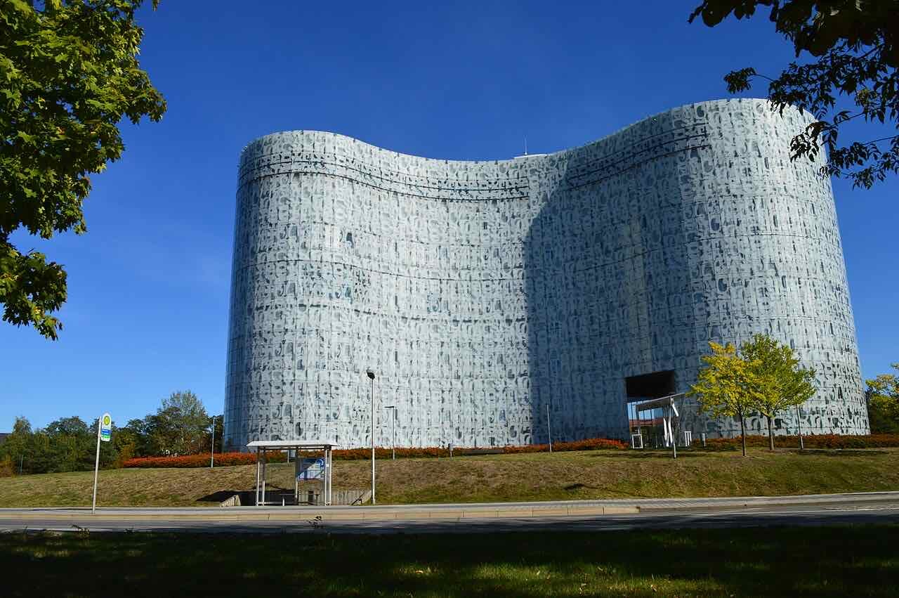 The curved, glass-fronted university library of the BTU printed with a pattern of letters, under a blue sky