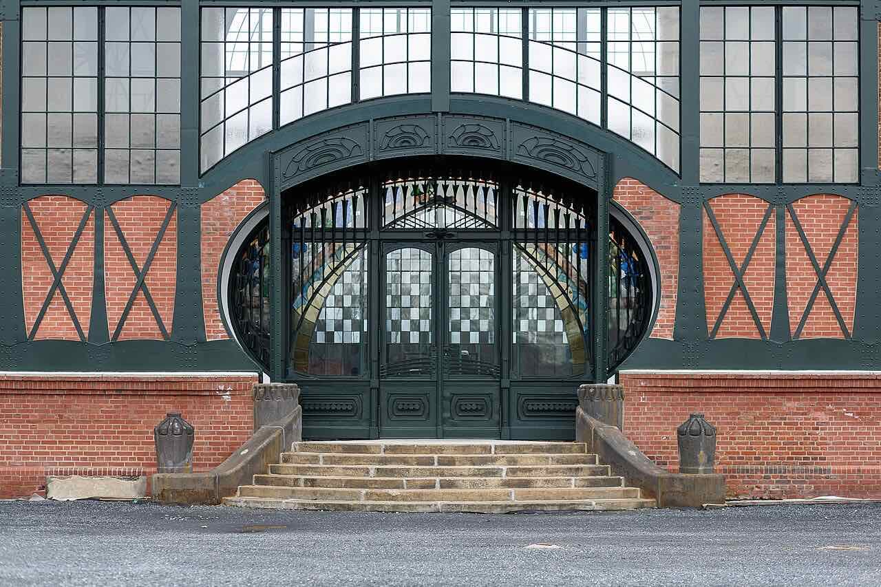 The green iron and red-brick entrance portal of a machine hall with stone steps and glass doors