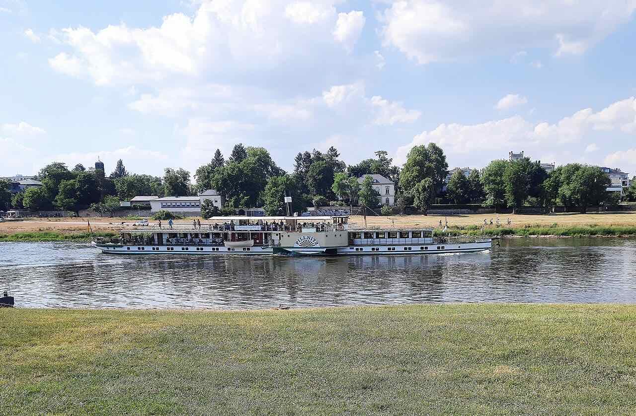 A white paddle steamer on the Elbe in Dresden on a sunny day, with green meadows and villas on the far bank