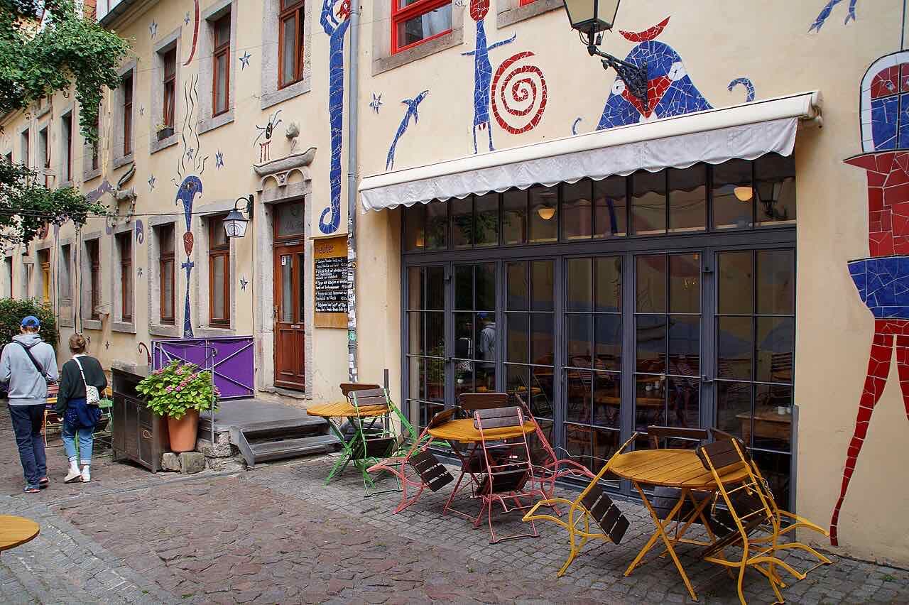A courtyard in the Kunsthofpassage in the Neustadt, with mosaic figures on the yellow facade and café tables on the cobbles