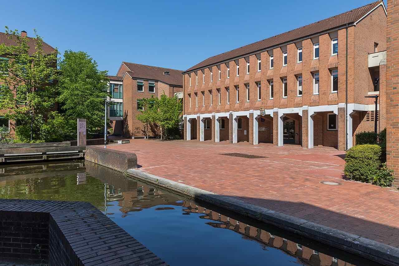 The brick library building of the Emden campus with a paved square and a canal in front on a sunny day