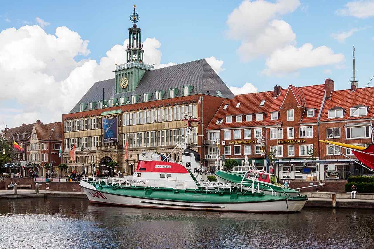 The Ratsdelft harbour basin in Emden with the green-roofed town hall tower behind, the museum rescue cruiser Georg Breusing and red-roofed brick houses on the quay