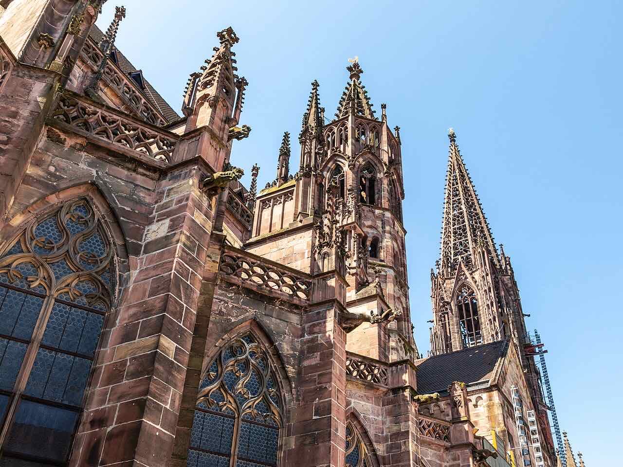 Red sandstone towers, pinnacles and tall traceried windows of Freiburg Minster against a blue sky