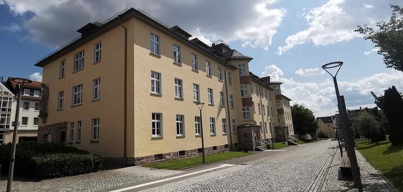 A yellow plastered building of Hochschule Fulda beside a cobbled campus lane under a sky of big clouds