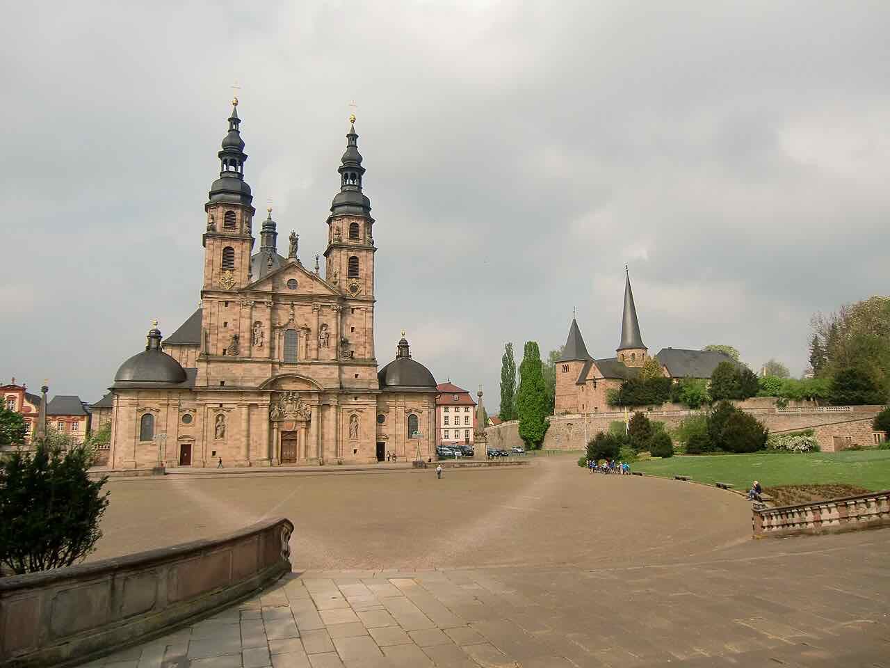 The cathedral square in Fulda seen from the side, with the pink sandstone cathedral on the left and the pointed spire of the Michaelskirche behind a wall on the right