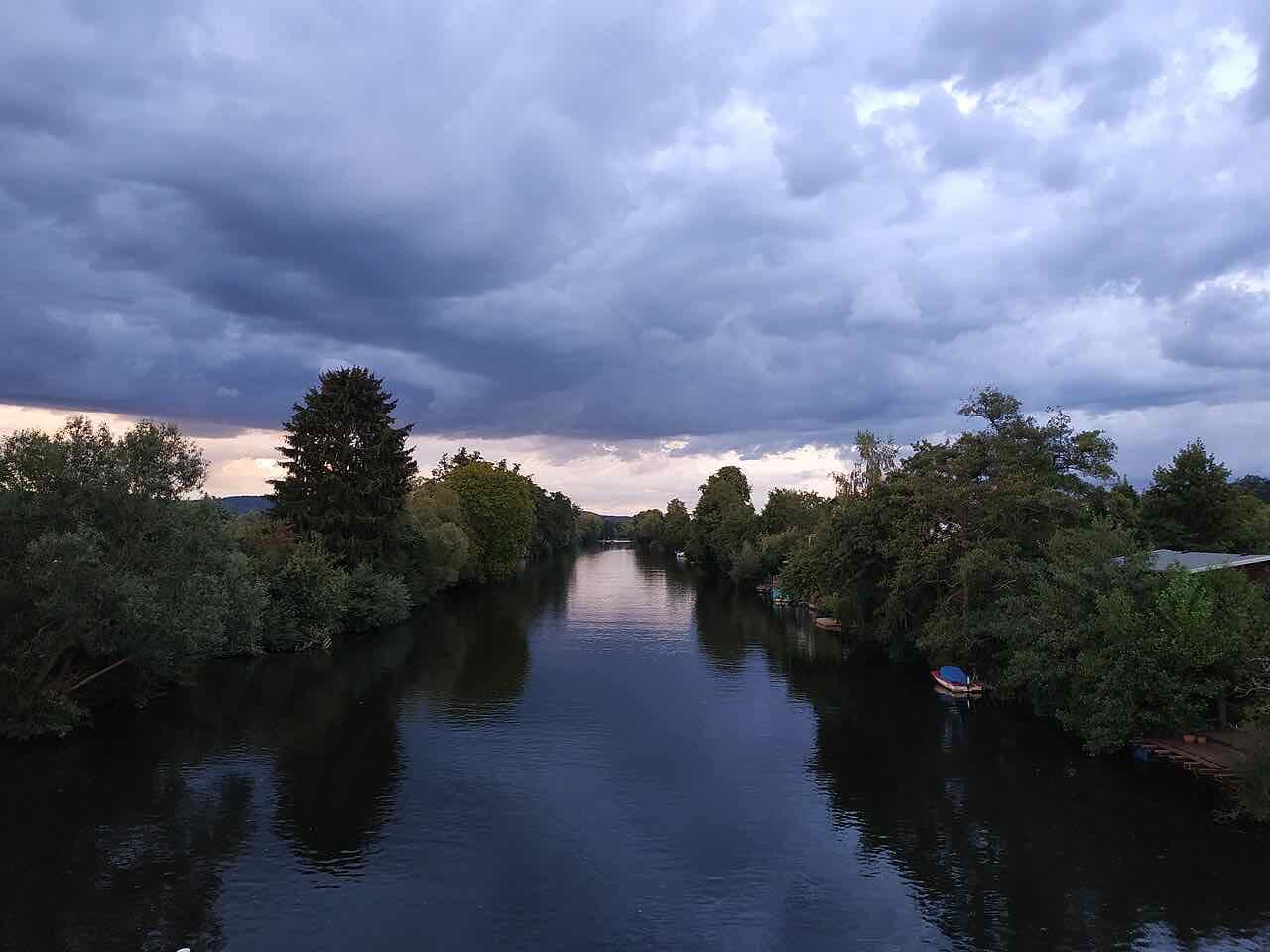The Lahn running straight between tree-lined banks under a dark evening sky, with small boats moored on the right bank
