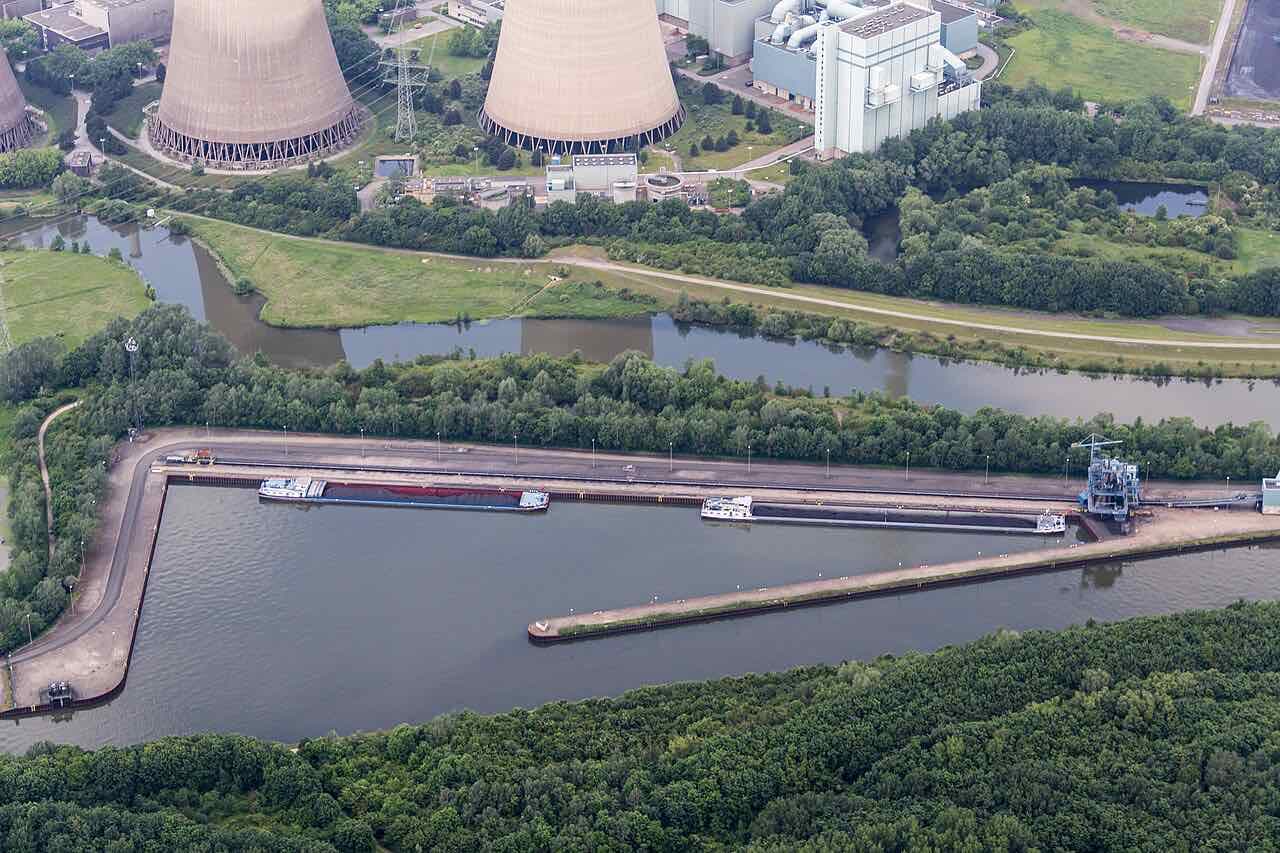 Aerial view of the Datteln-Hamm Canal with two cargo barges in a harbour basin beside cooling towers and a river