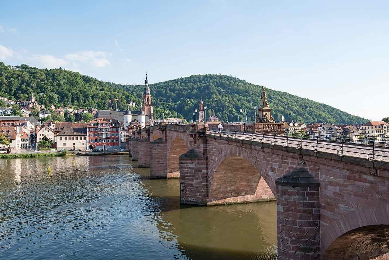 The Old Bridge seen from its roadway on a sunny day, with the old town, the church towers and a forested hill behind