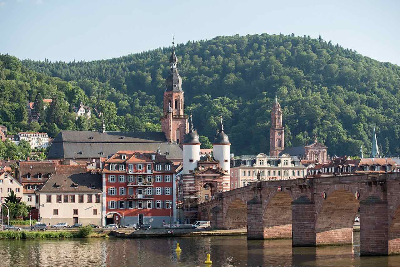 The twin-towered bridge gate at the old-town end of the Old Bridge, with church towers and a wooded hill behind