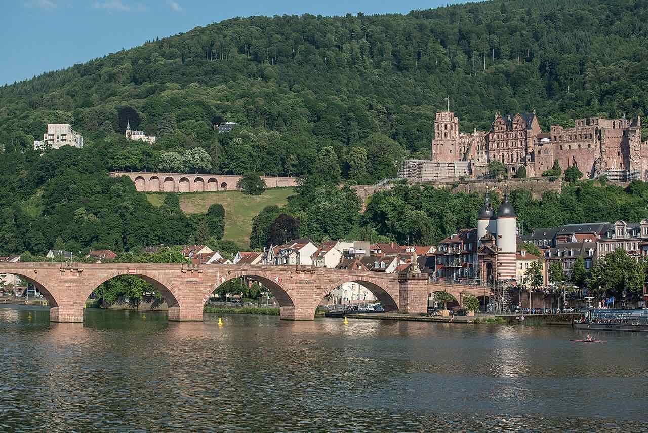 The red sandstone arches of the Old Bridge over the Neckar, the bridge gate and the ruined Heidelberg Castle above the town on a wooded hillside