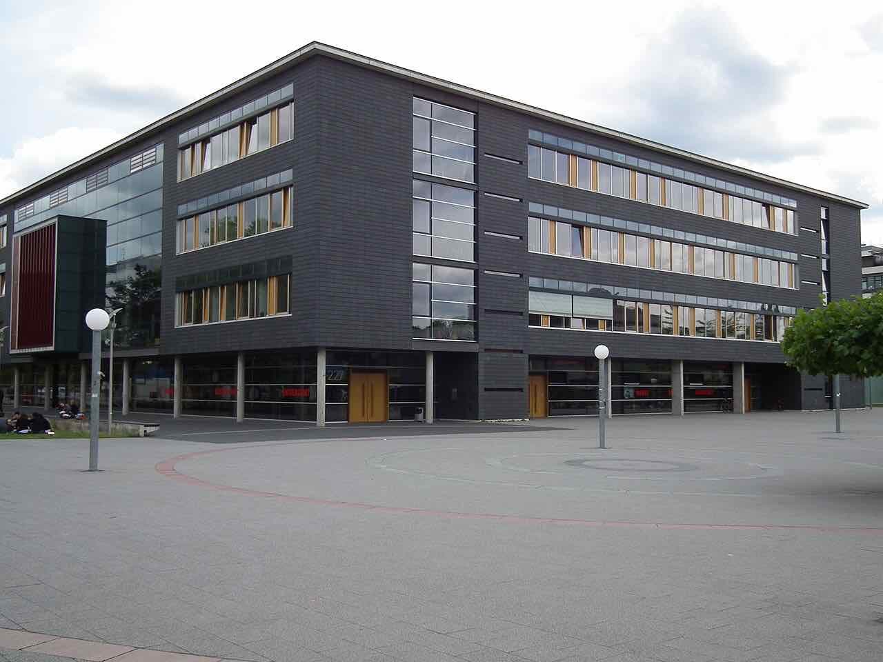 A dark slate-clad university building with a large paved square in front on the Neuenheimer Feld campus