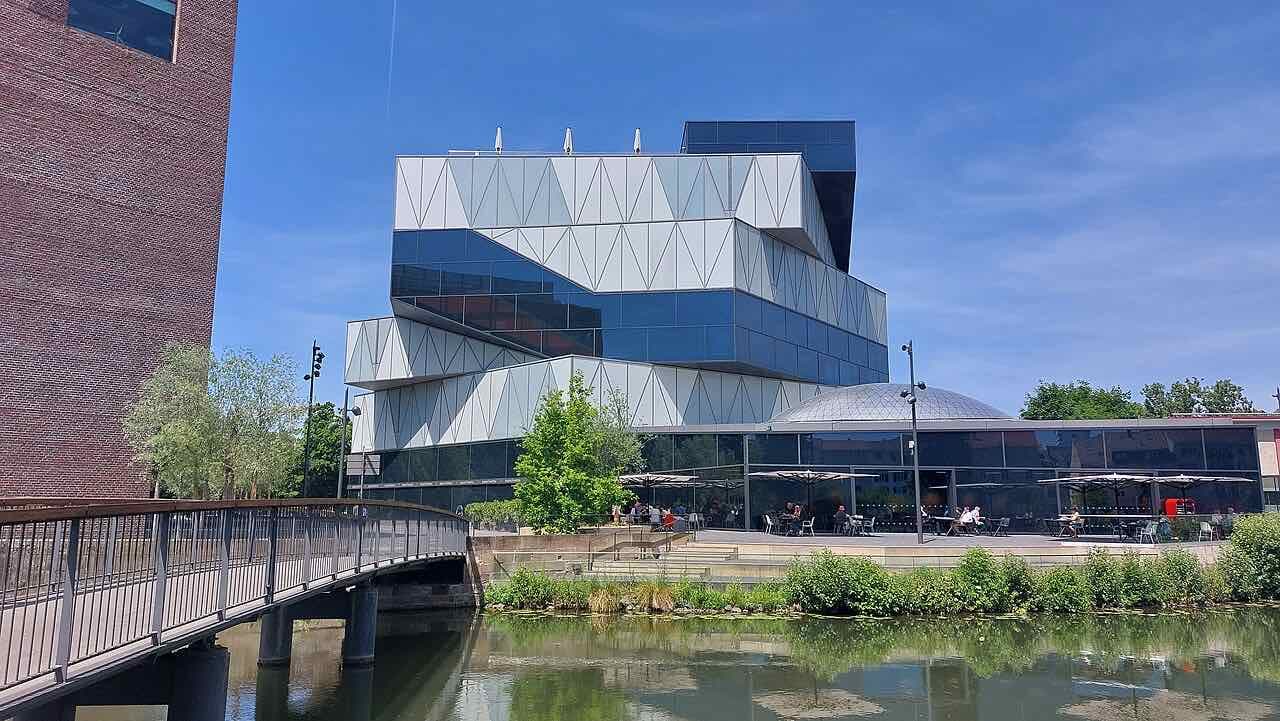The experimenta science center, a stacked glass and white-panel building with a dome beside it, across the water with a footbridge and a terrace