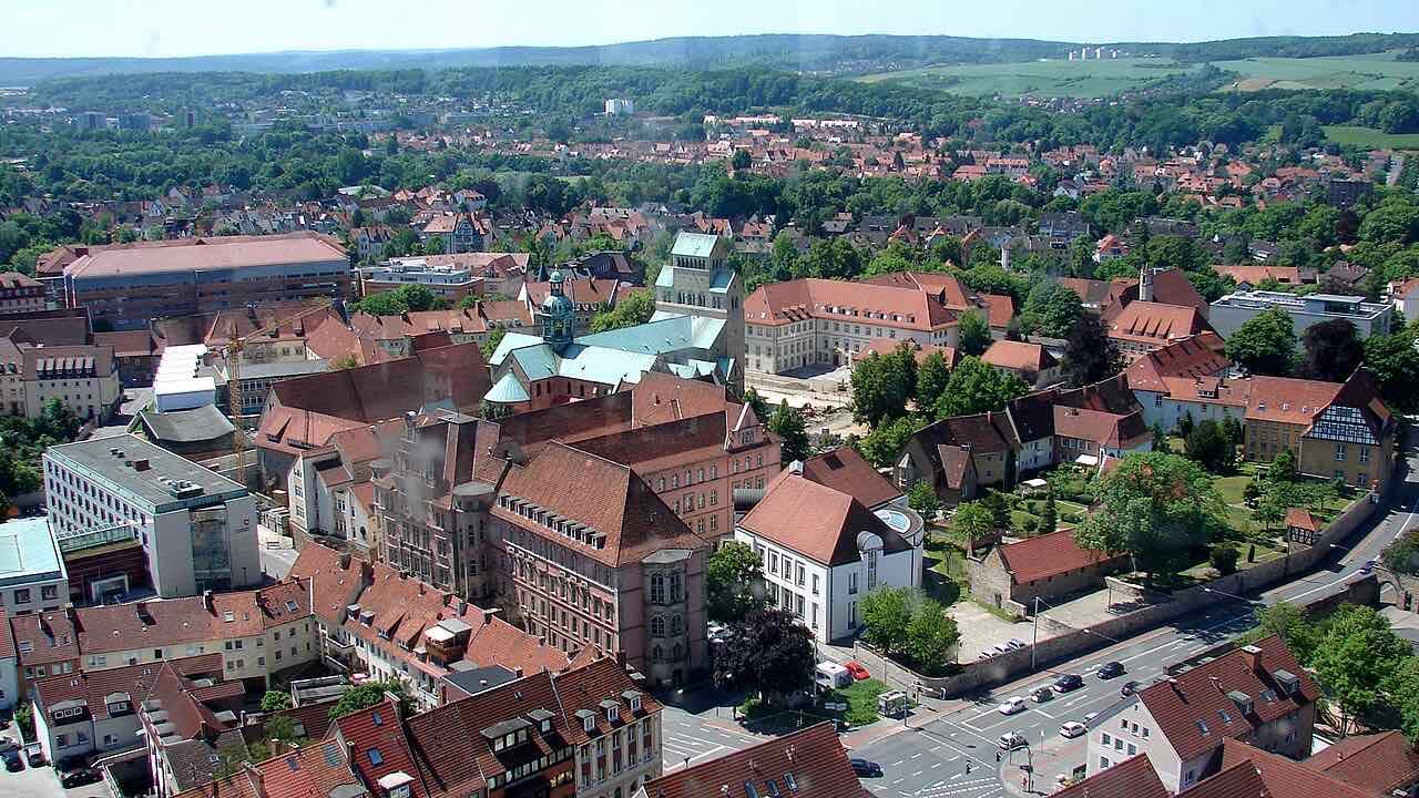 View over the red roofs of Hildesheim from the St. Andreas tower, with the cathedral's green roofs in the middle and wooded hills behind