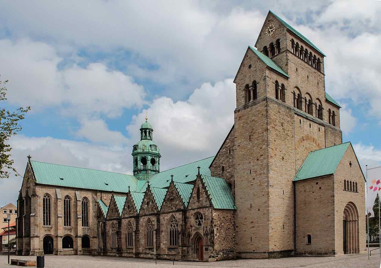 The Hildesheim Mariendom seen from the side, a sandstone cathedral with a heavy west tower and green copper roofs