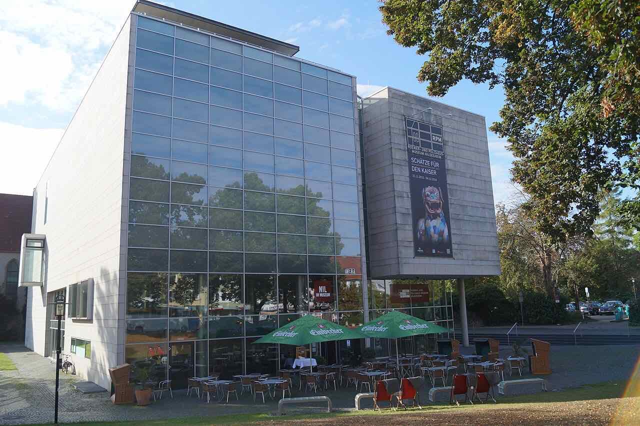 The glass-fronted extension of the Roemer- und Pelizaeus-Museum with a café terrace and green parasols in front