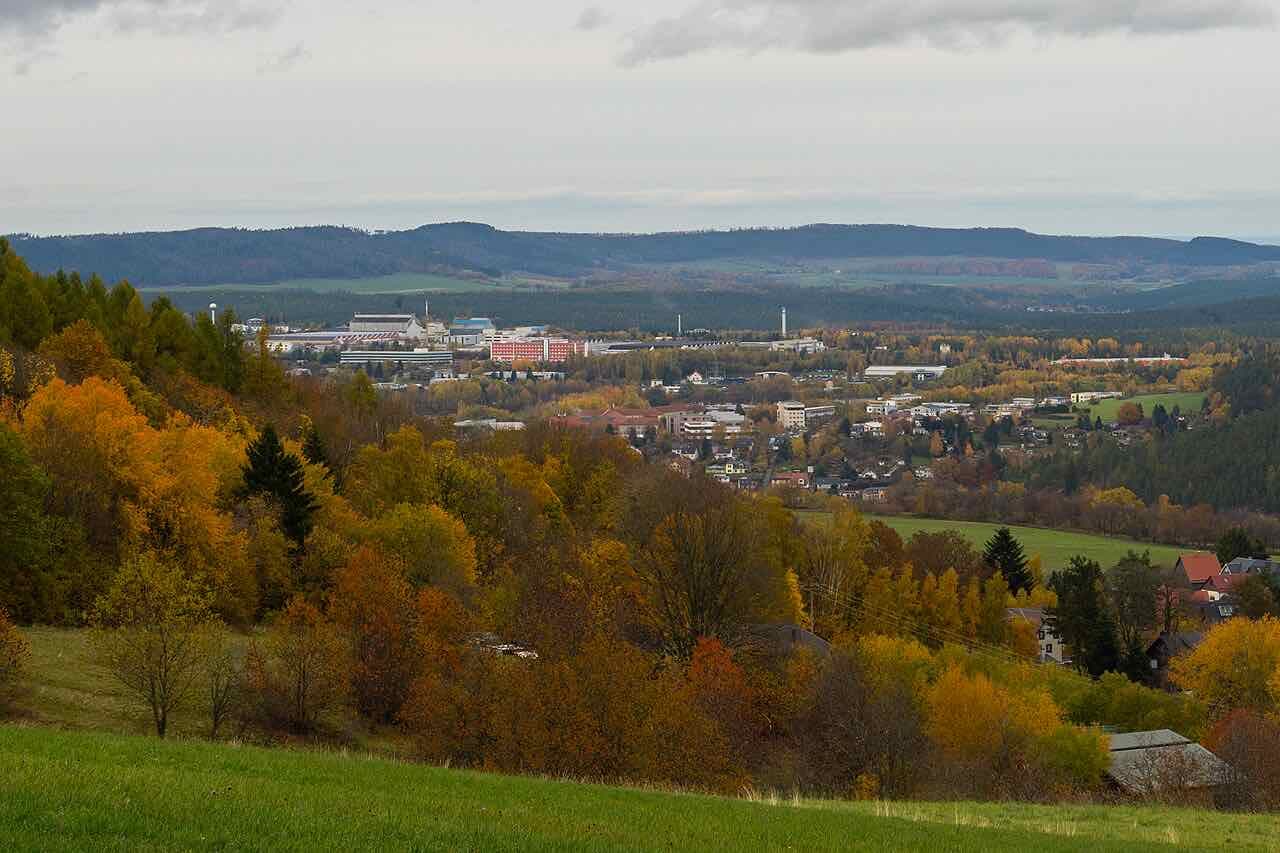 Ilmenau seen from a hillside meadow in autumn, with the town in the valley and the forested ridge of the Thuringian Forest behind it
