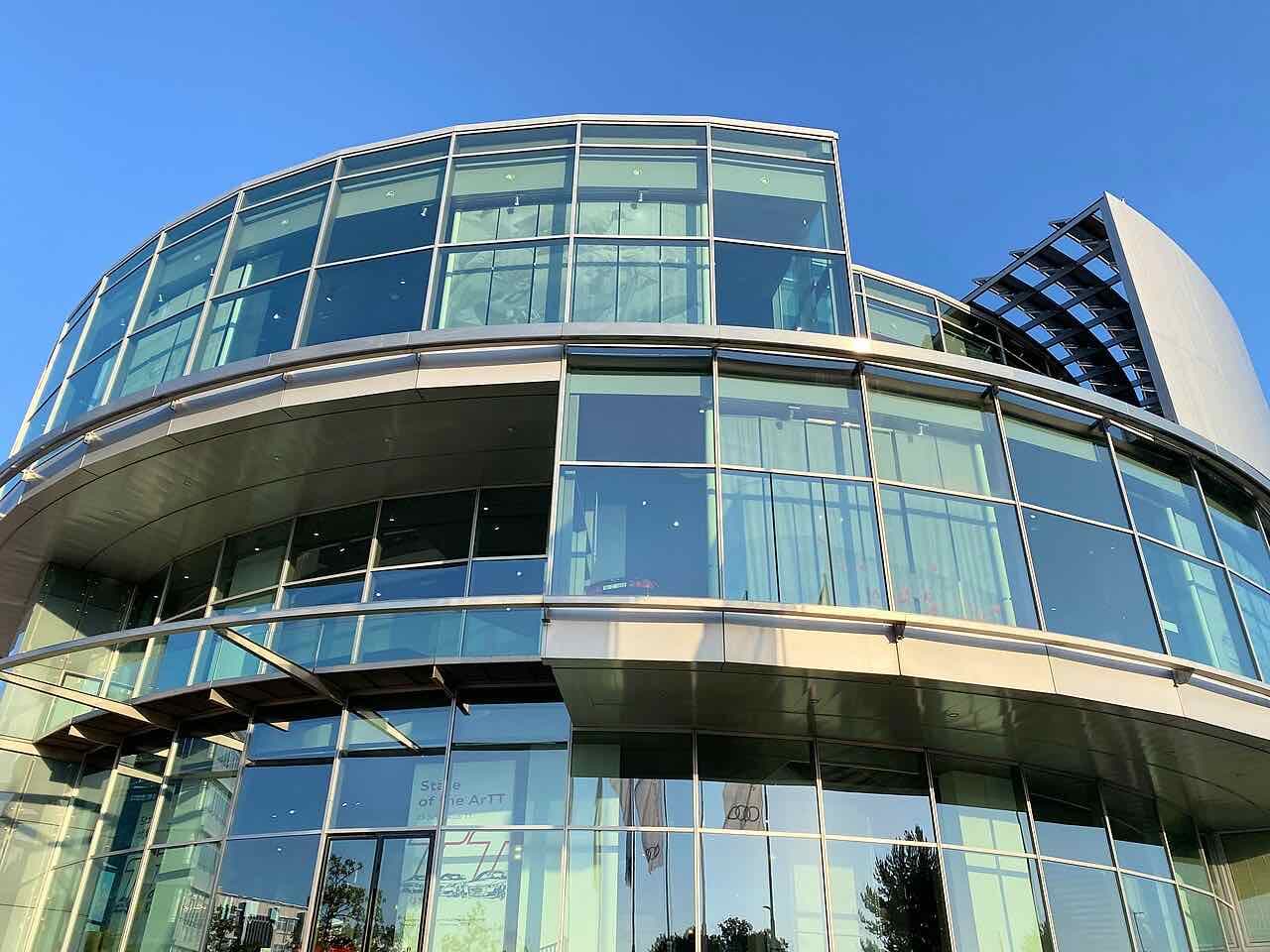The curved glass and steel front of the Audi Forum in Ingolstadt against a clear blue sky