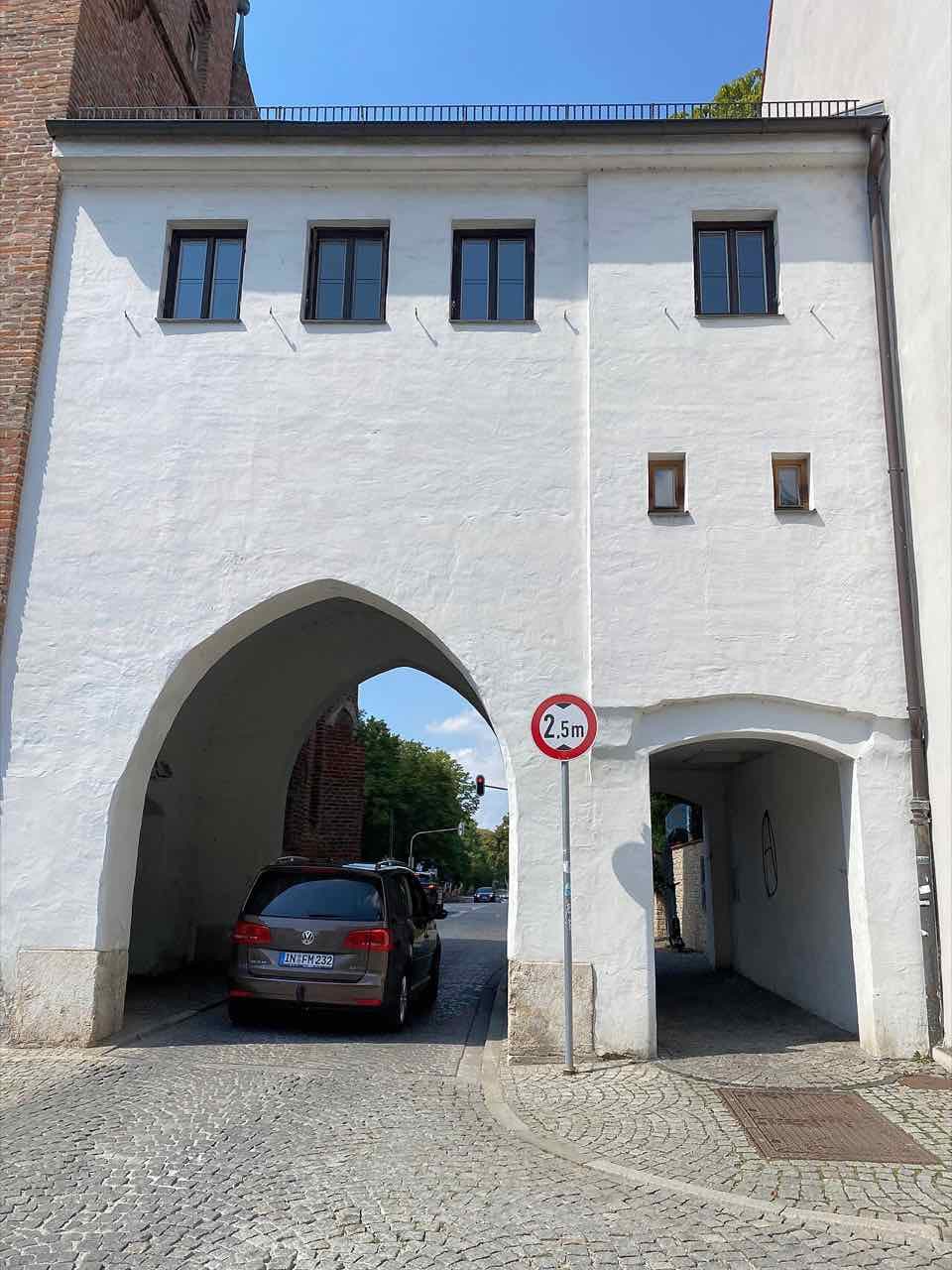 The whitewashed Kreuztor gate with a pointed arch and a car driving through it onto a cobbled street