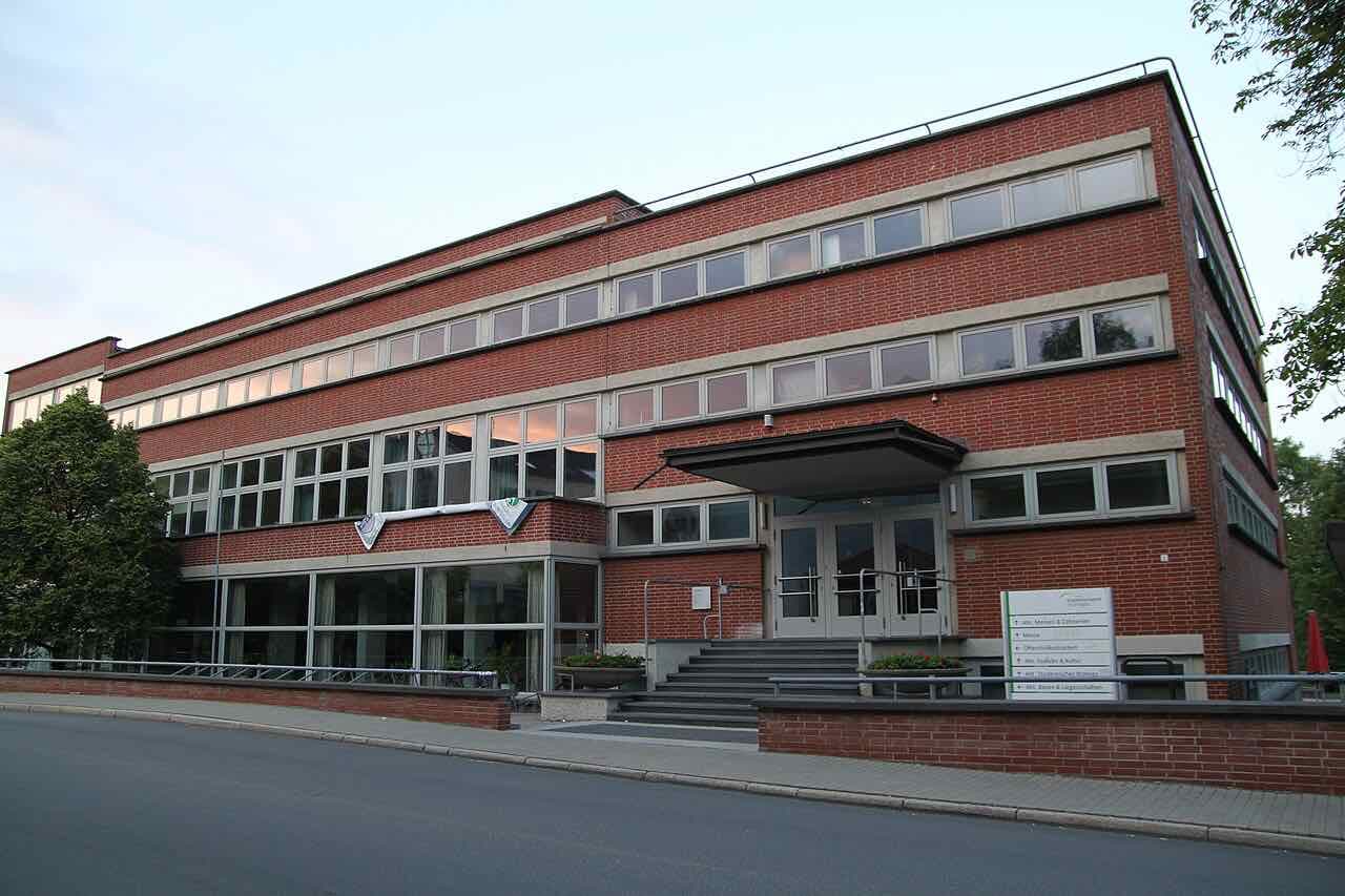 The red-brick building of the Philosophenweg canteen at dusk, with a small canopy over the entrance and a quiet street in front