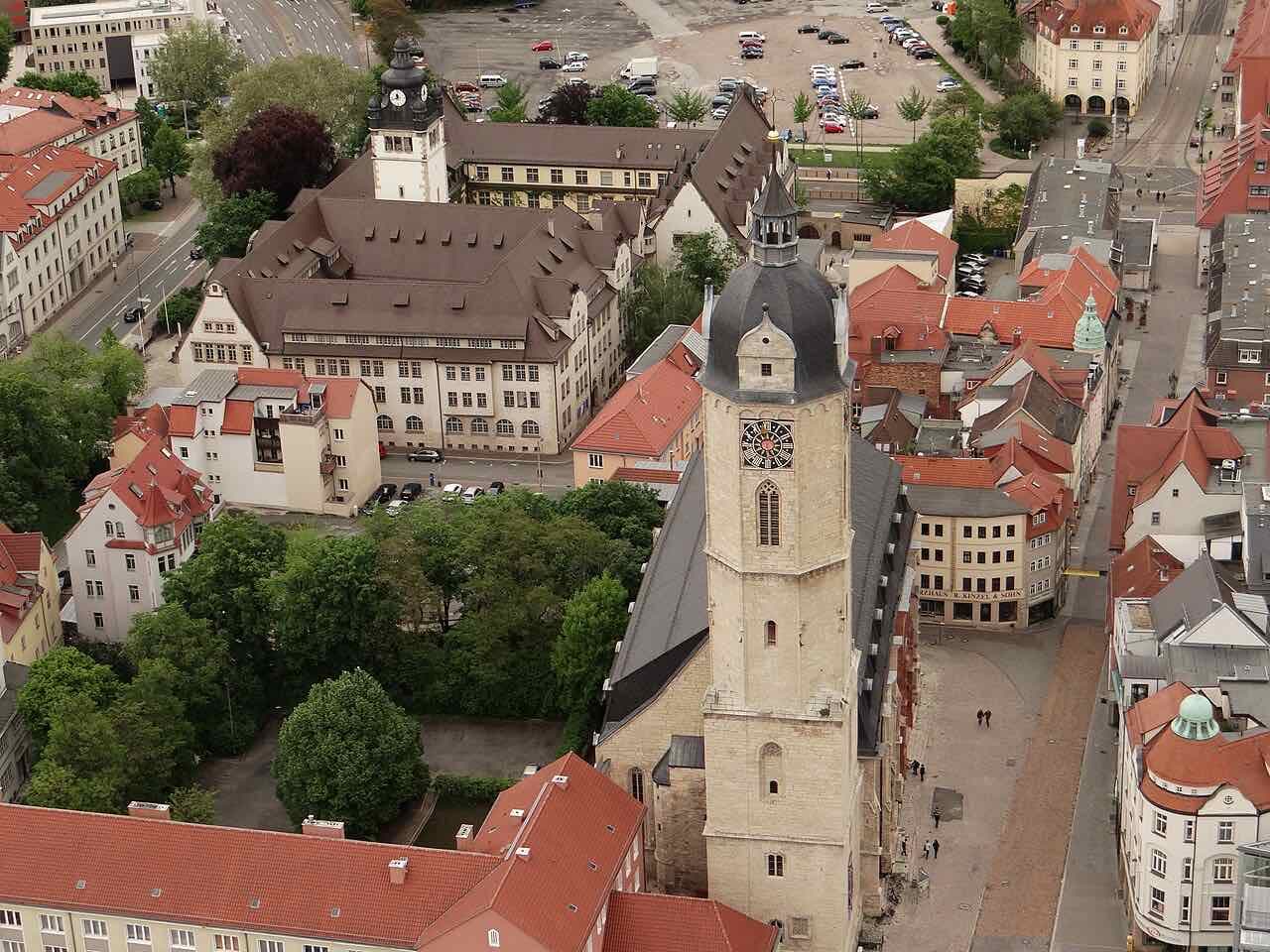 The clock tower of the Stadtkirche St. Michael seen from above, with old town buildings, a small square and a car park around it