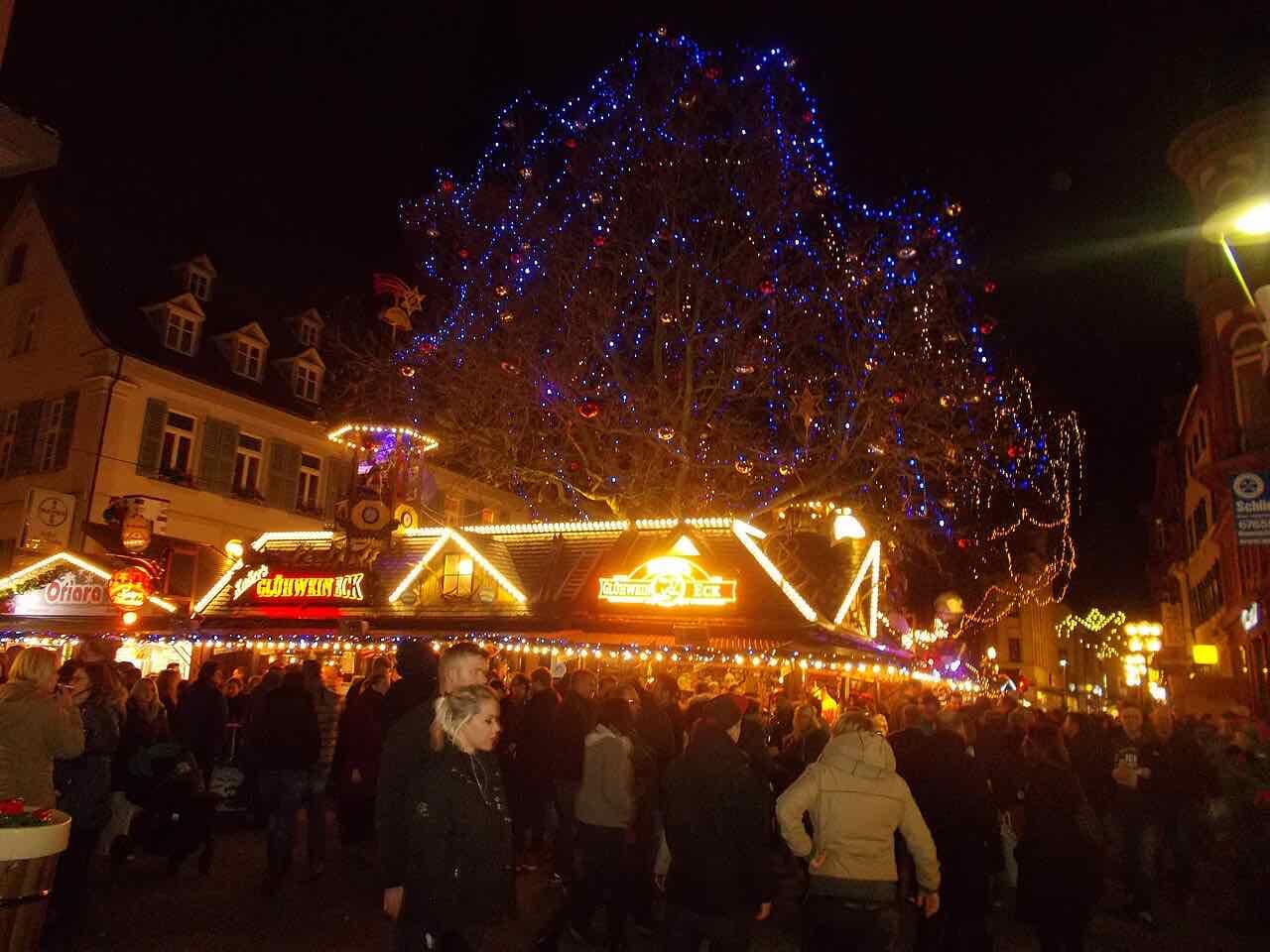 The Christmas market below the Stiftskirche at night, with wooden stalls, string lights and a large tree lit in blue