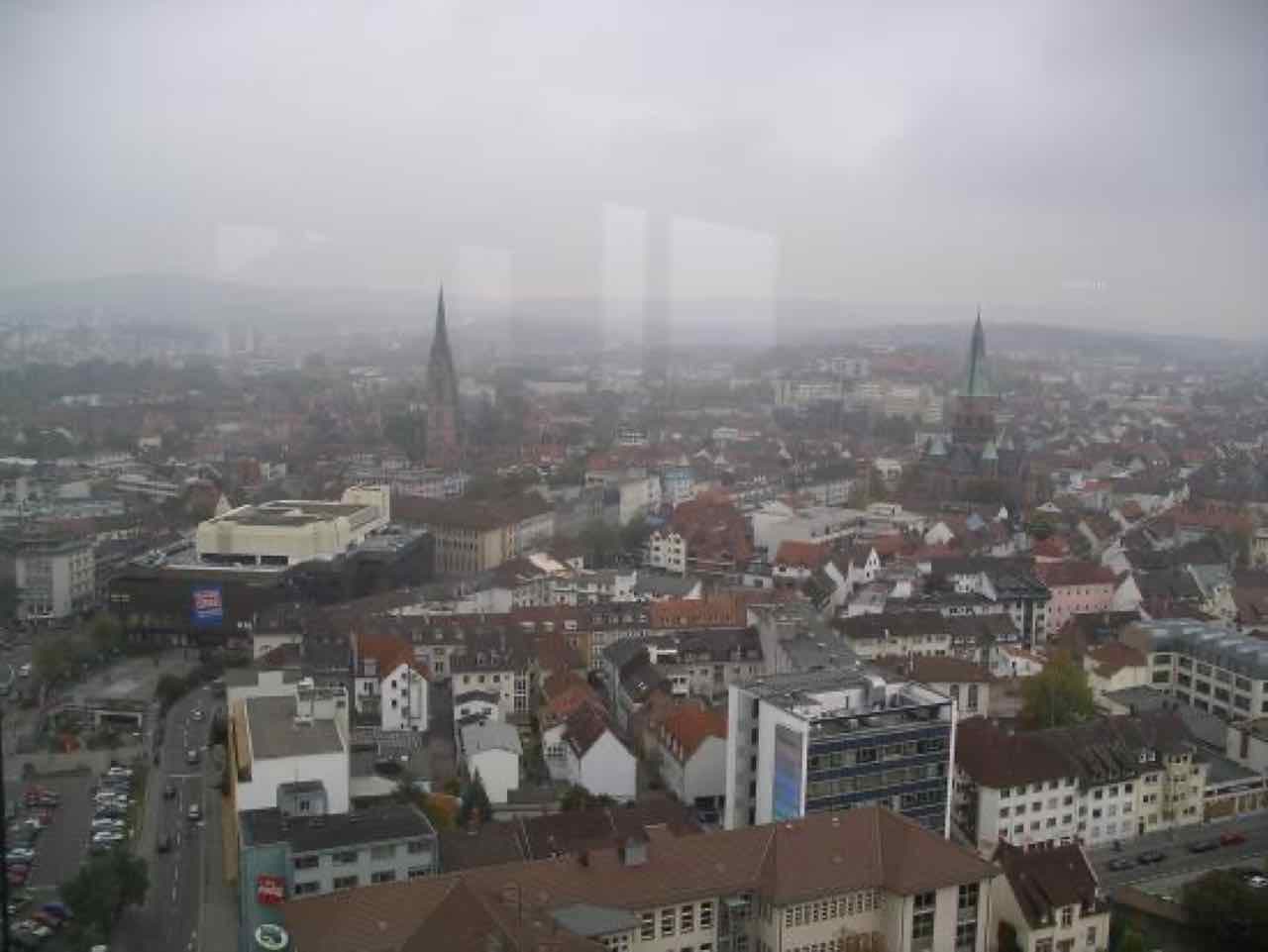 Hazy aerial view over the roofs of central Kaiserslautern with two church spires and low hills in the distance