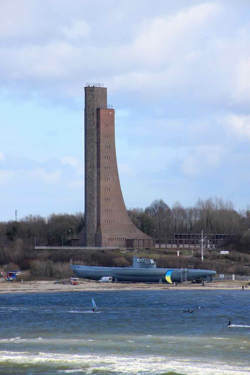 The tall brick tower of the Laboe naval memorial above the shore, with the submarine U-995 on the beach and windsurfers in the surf