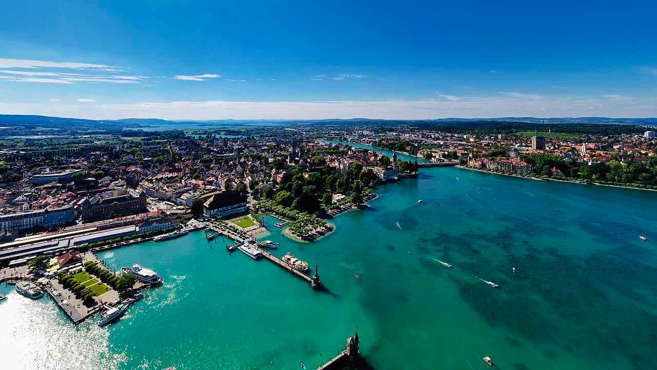 Aerial view of Konstanz harbour, with the old town on the left, ships at the piers, the Rhine leaving the lake and the Swiss shore beyond