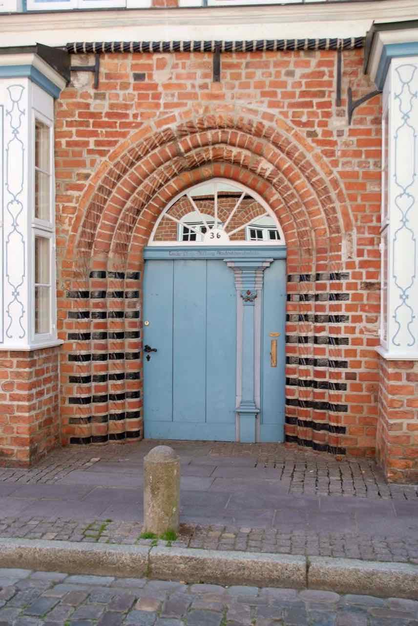 A blue wooden door in a red-brick arched doorway on a cobbled street in the old town, number 36, with a student hall inscription above the door