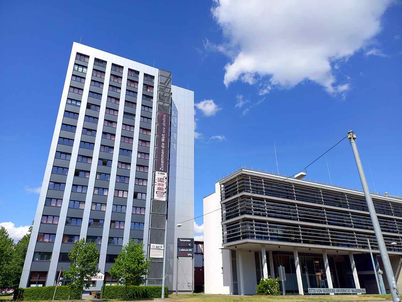 A tall student residence tower beside the glass-fronted Faculty of Electrical Engineering and Information Technology on the OVGU campus under a blue sky
