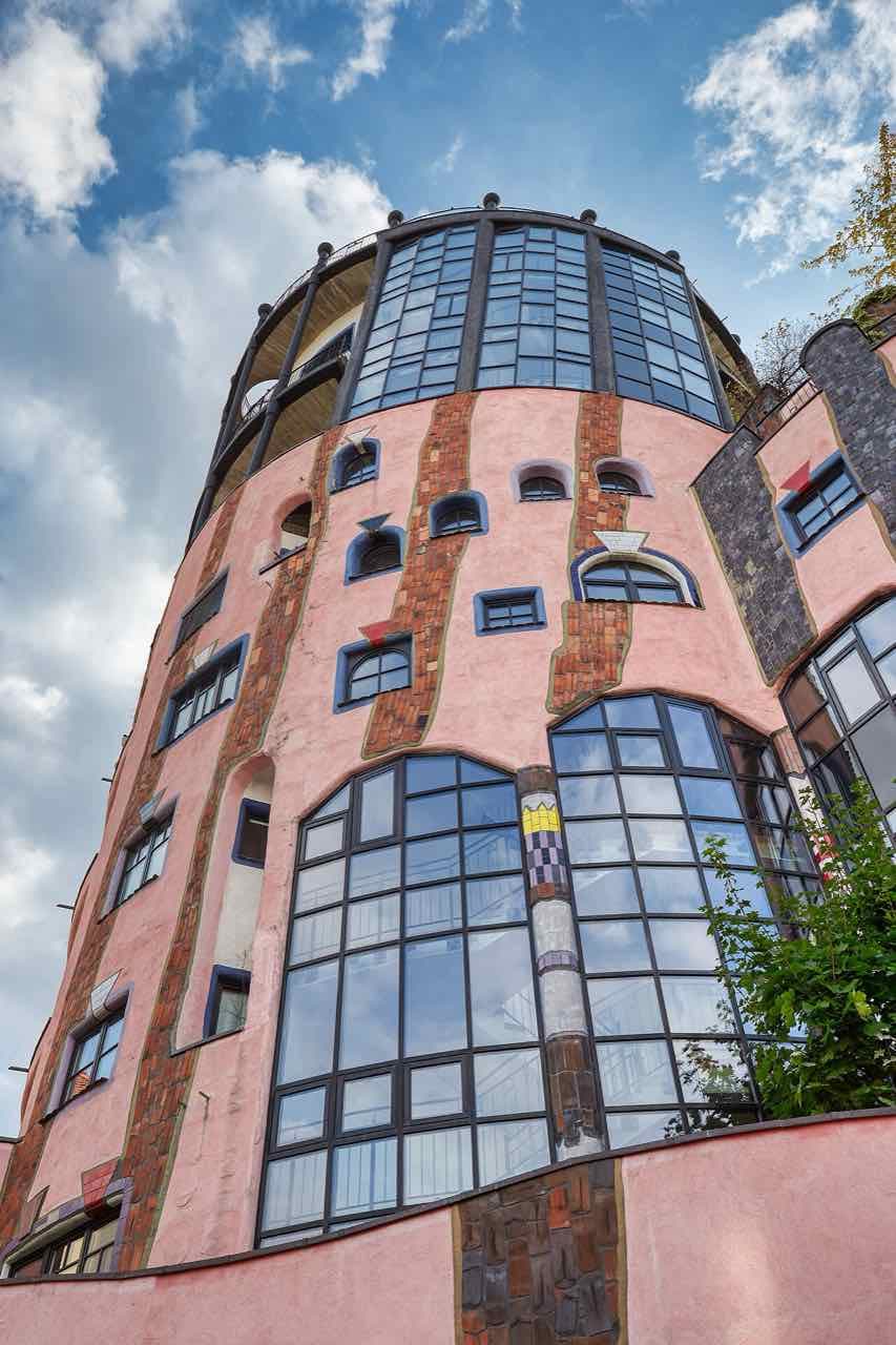 The coloured, curving facade and tower of Hundertwasser's Green Citadel in Magdeburg, with trees on the roofs
