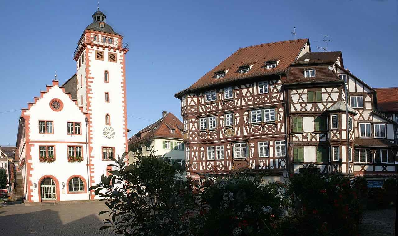 The white Rathaus with its red-trimmed tower on the left and the dark half-timbered Palm'sches Haus on the right, on the Marktplatz of Mosbach under a blue sky