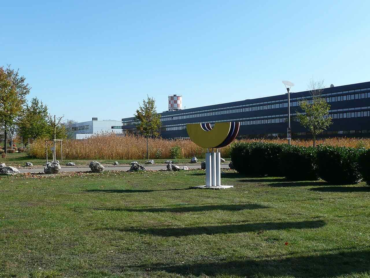 Reeds and a lawn along the lake next to the main building of the Hochschule Neu-Ulm, with a small sculpture on the grass