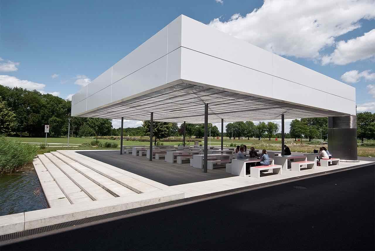 The white roofed terrace of the HNU canteen beside the campus lake, with tables, stepped seating and trees behind