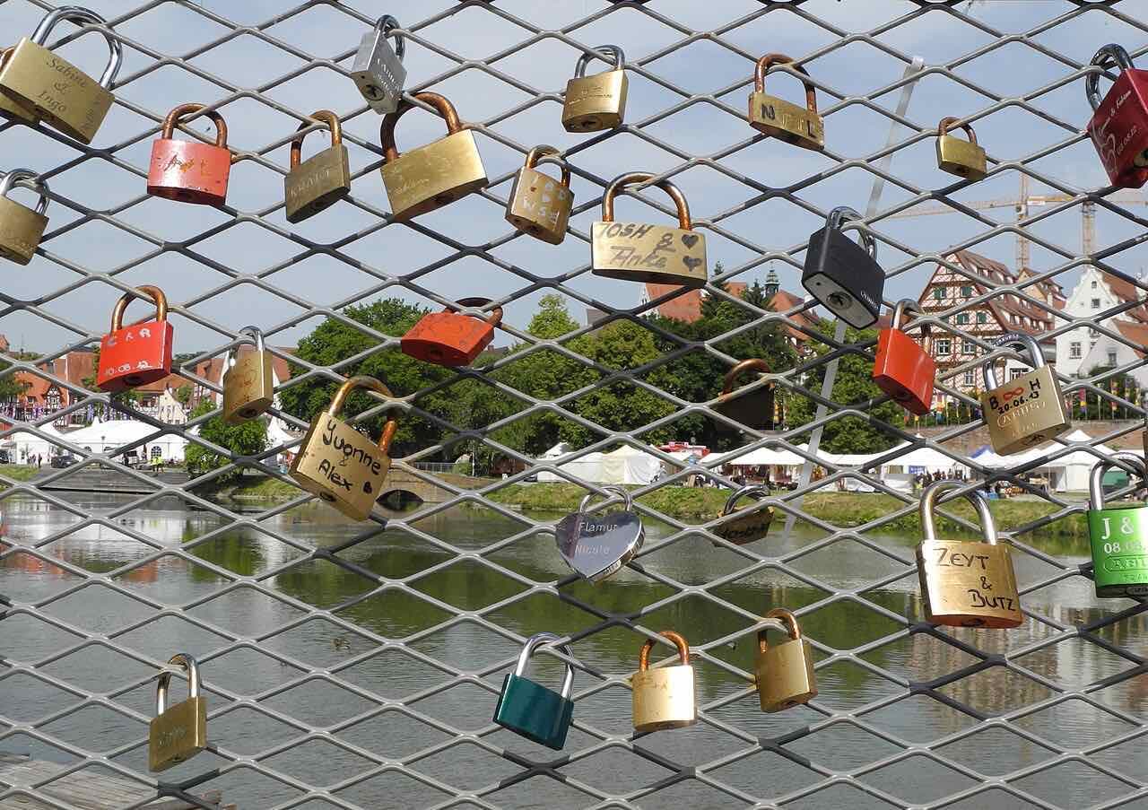 Colourful padlocks on a wire-mesh railing at the Jahnufer in Neu-Ulm, with the riverbank and buildings of Ulm behind