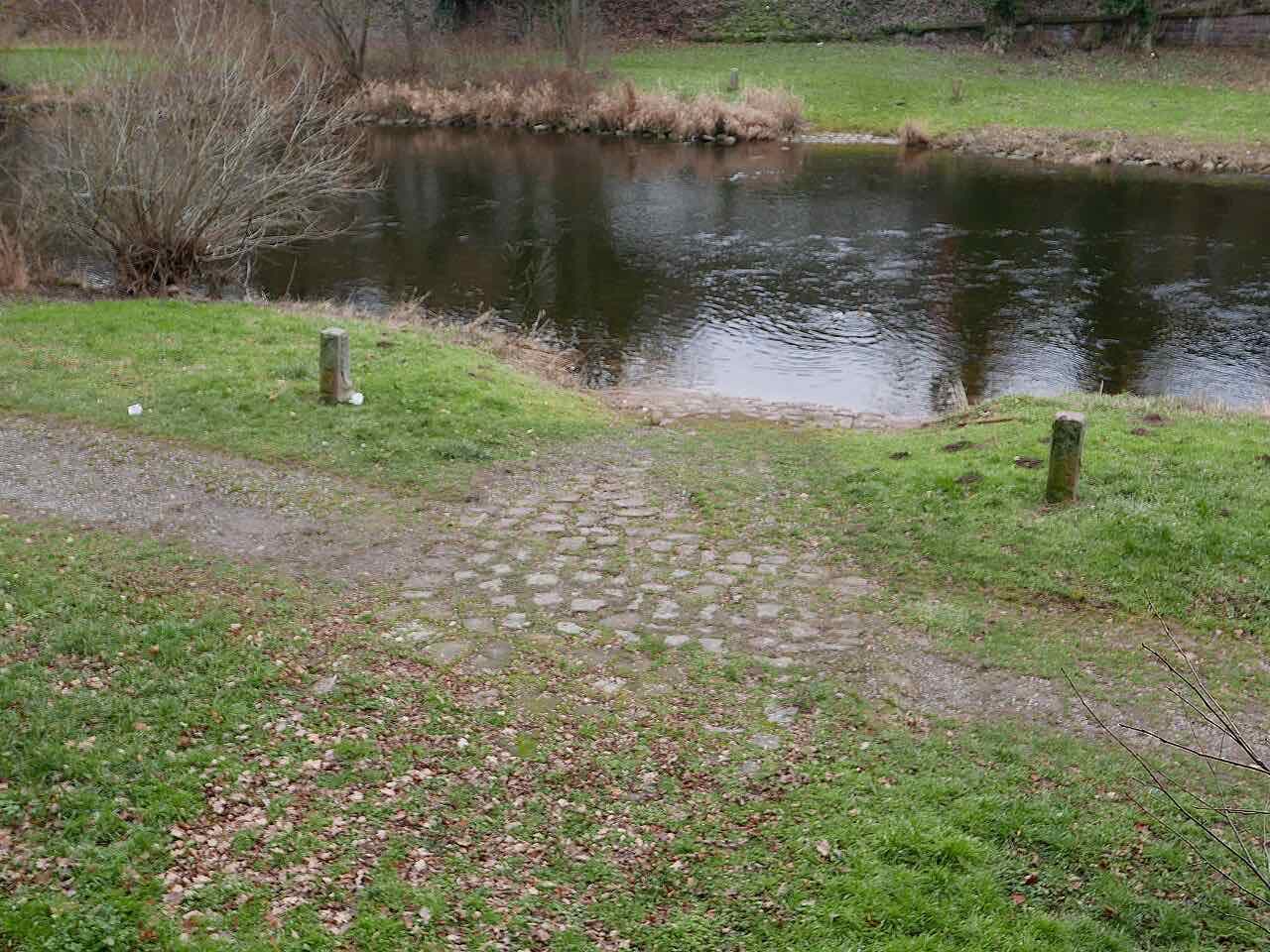 A cobbled ramp leading down through grass into the river Enz, a reconstruction of the old Roman ford