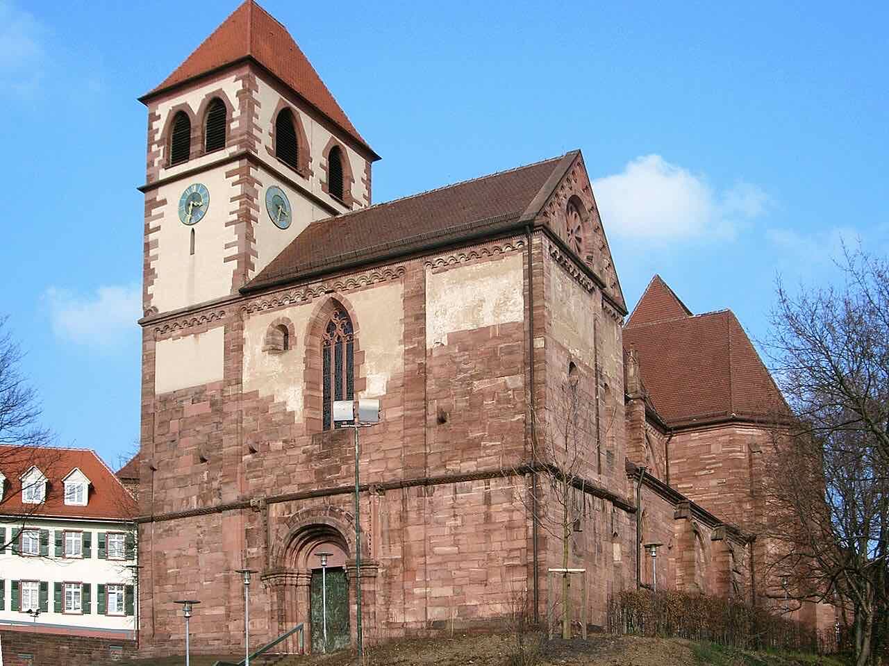 The red sandstone Schlosskirche St. Michael with its square clock tower and round-arched Romanesque doorway against a blue sky