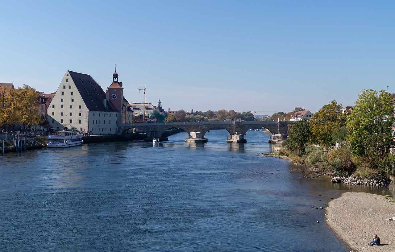 The Stone Bridge crossing the Danube beyond the Salzstadel and the bridge tower, with a river boat at the quay and autumn trees